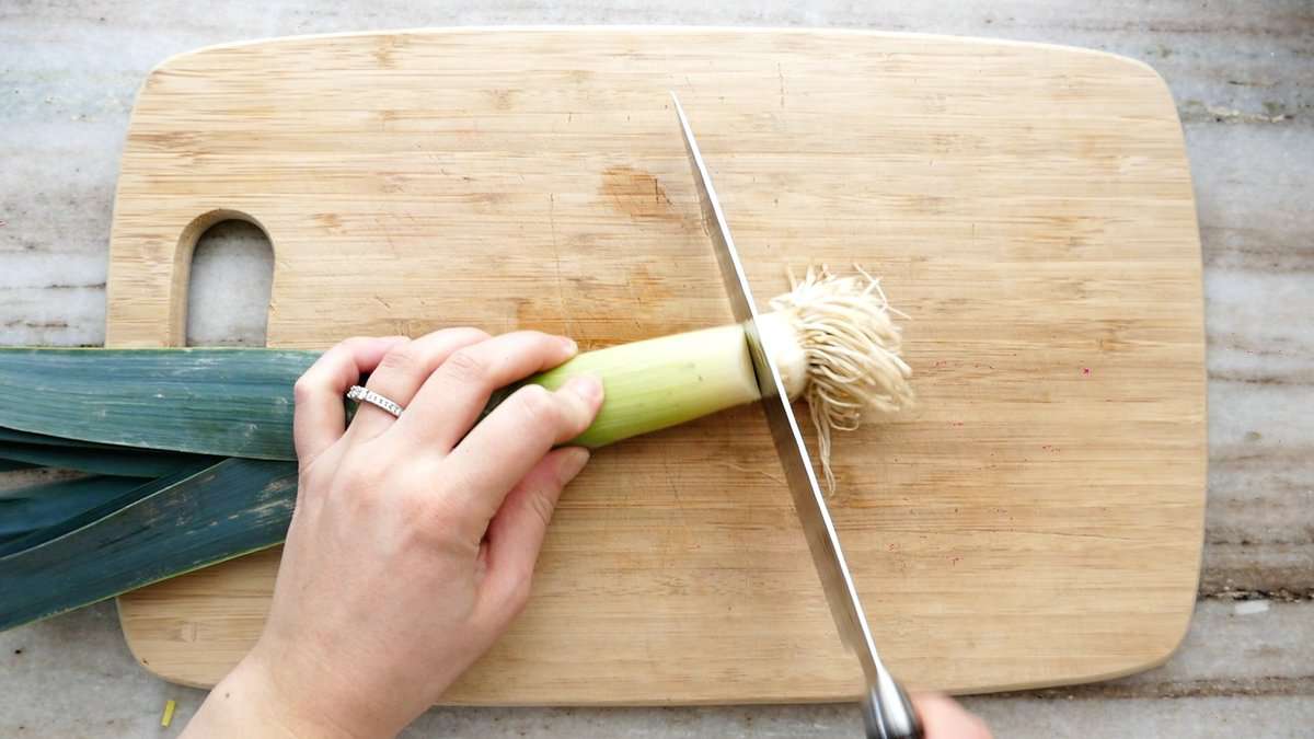 woman trimming off the root of a leek on a cutting board