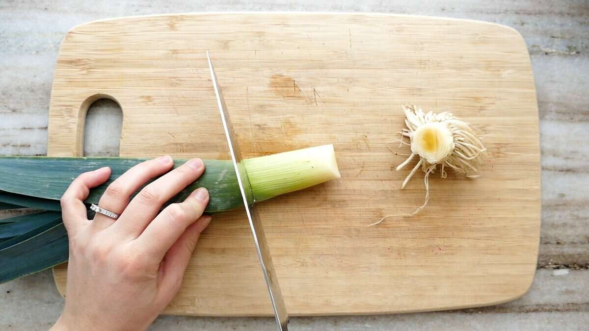woman trimming off the green part of a leek on a cutting board