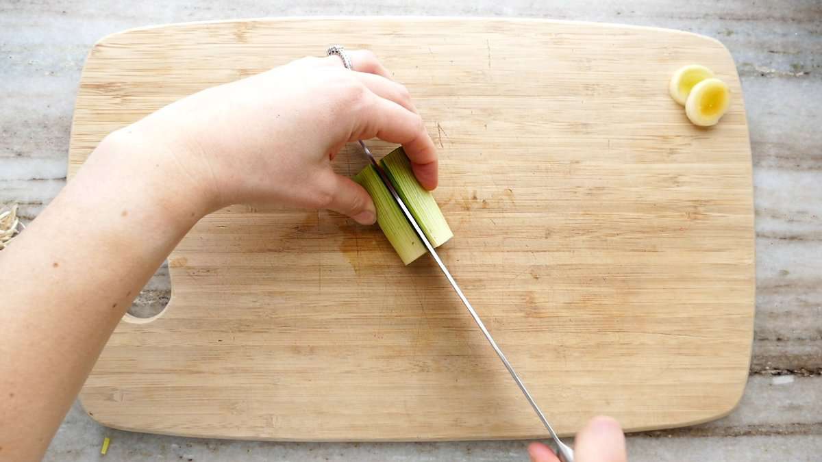 woman slicing a leek in half lengthwise on a cutting board