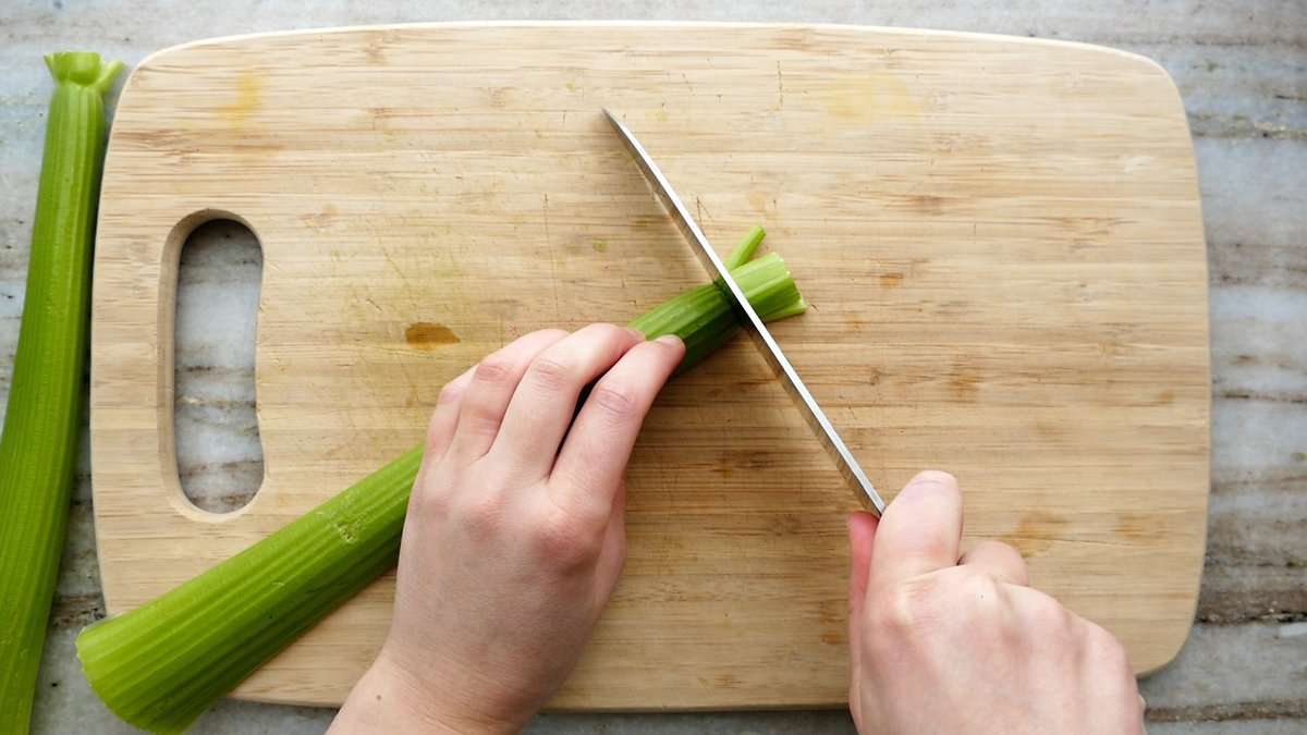 woman trimming off the joint of a celery stalk on a cutting board