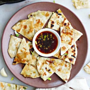 leek pancakes sliced into triangles on a plate with dipping sauce in the middle