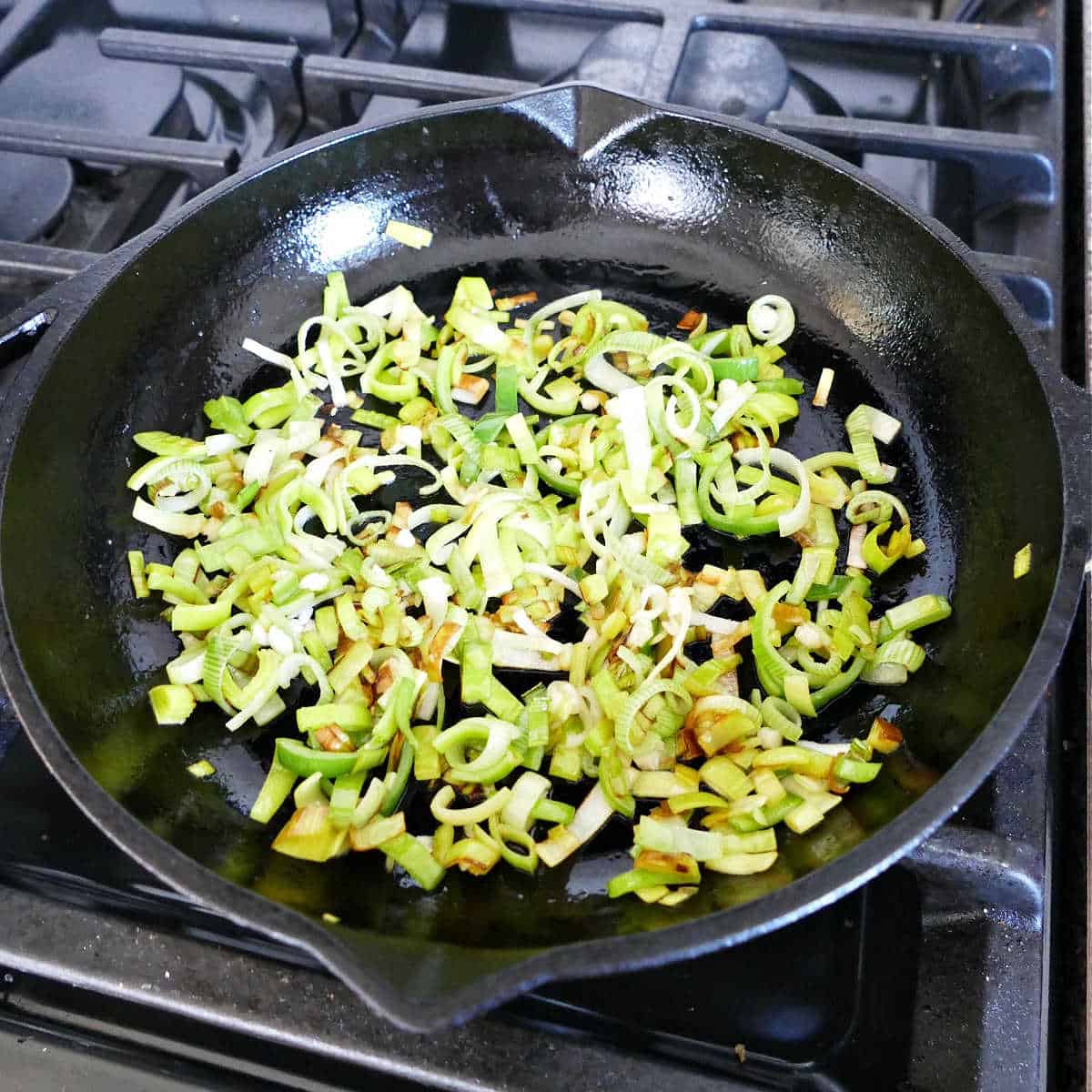 sliced leeks cooking in oil in a cast iron skillet