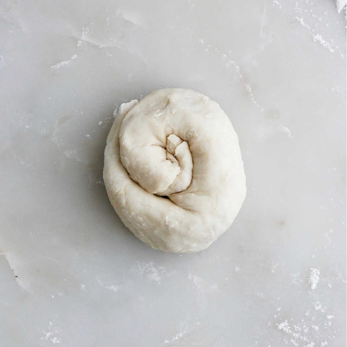 dough for leek pancakes rolled up into a spiral on a floured surface