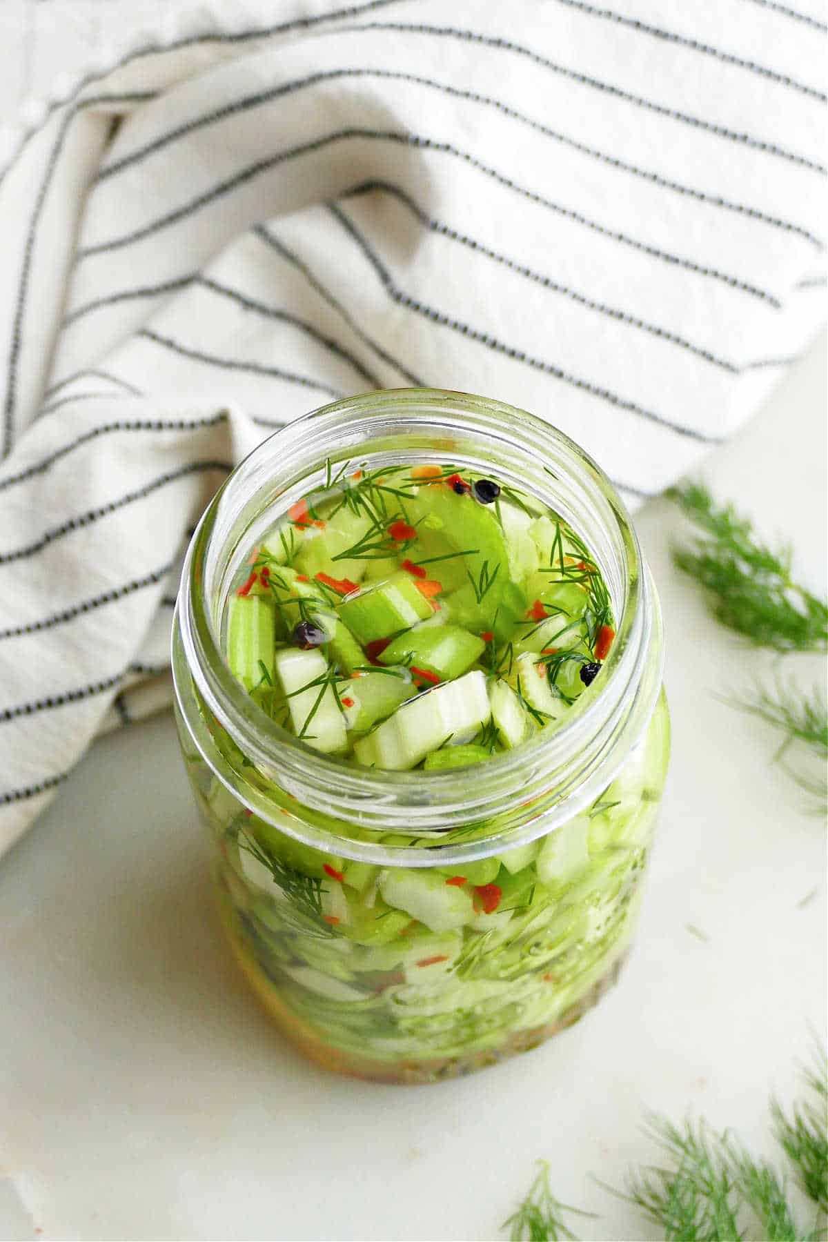 pickled celery in a jar next to a striped napkin and fresh dill