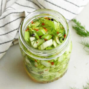 pickled celery in a jar next to a striped napkin and fresh dill