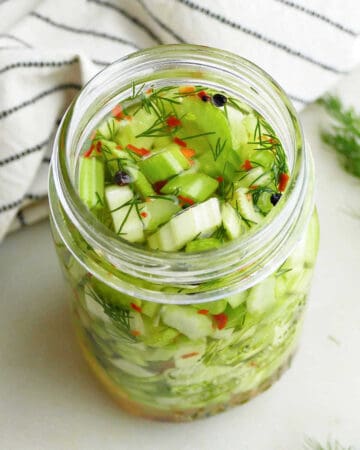 pickled celery in a jar next to a striped napkin and fresh dill