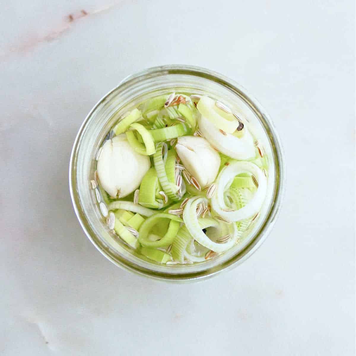 pickled leeks with seasonings in a jar before being put in the fridge
