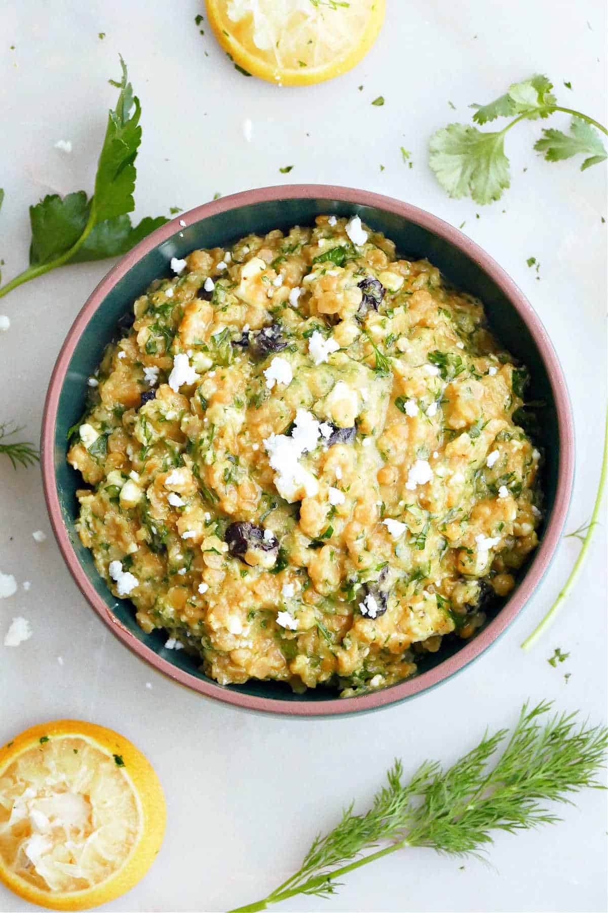 red lentil salad in a mixing bowl surrounded by herbs and lemons