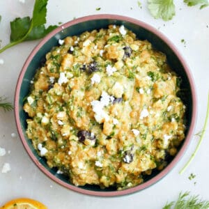 red lentil salad in a mixing bowl surrounded by herbs and lemons