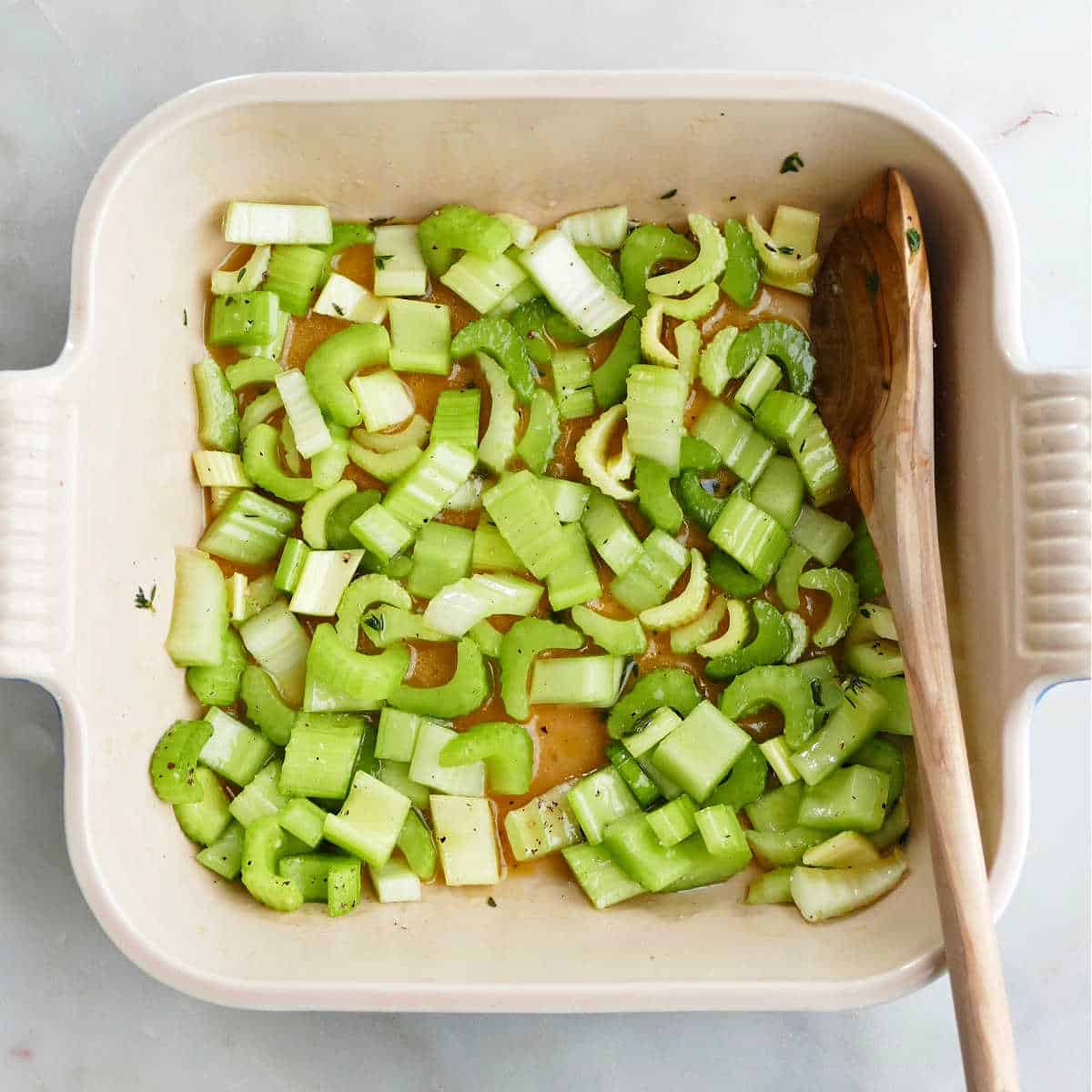 sliced celery mixed with olive oil, broth, and seasonings in a baking dish