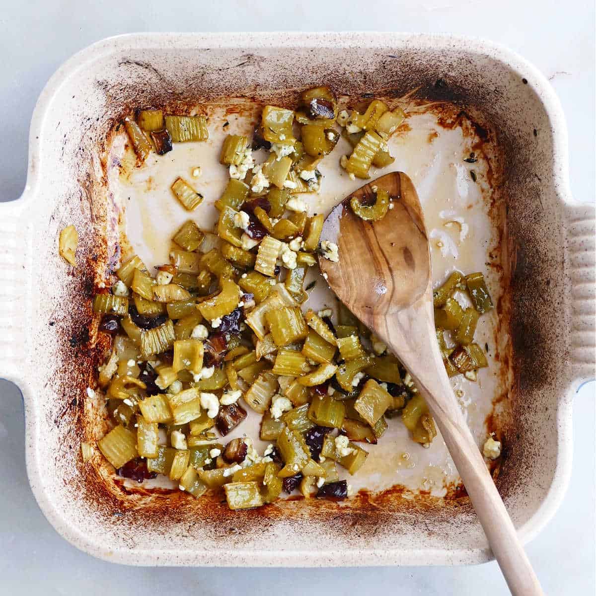 roasted celery being mixed with sliced dates and blue cheese in a baking dish