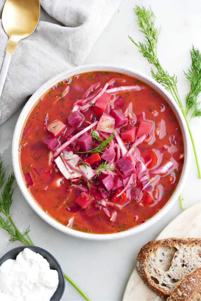 slow cooker borscht in a serving bowl next to dill, sour cream, and bread