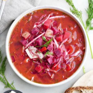 slow cooker borscht in a serving bowl next to dill, sour cream, and bread