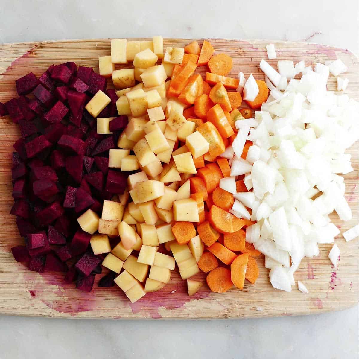 chopped beets, potatoes, carrots, and onion on a bamboo cutting board