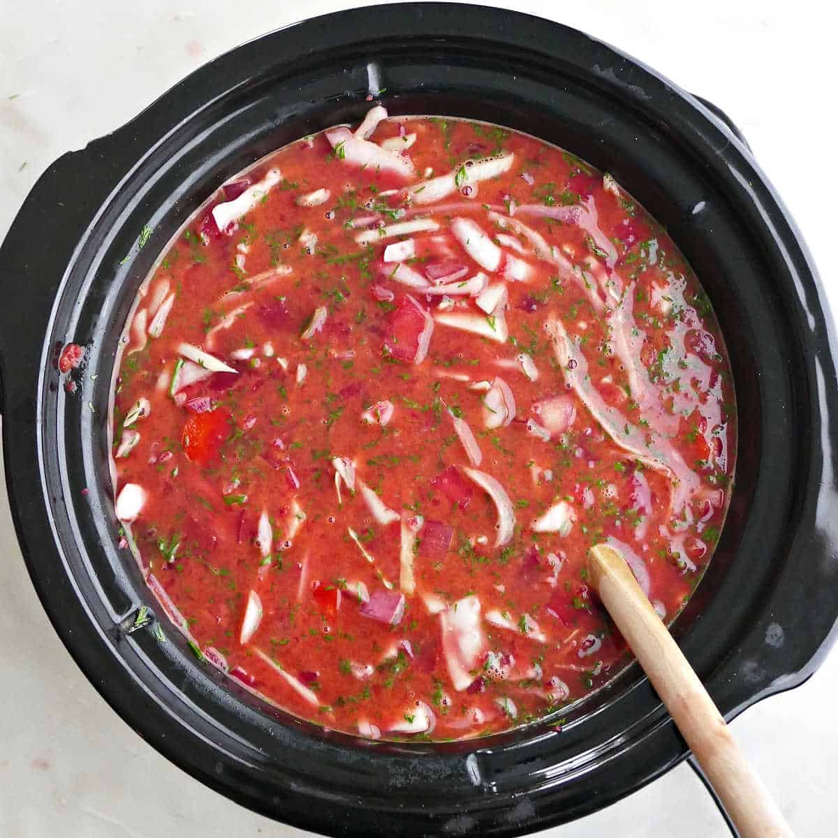 cooked borscht in a slow cooker with cabbage being stirred into it