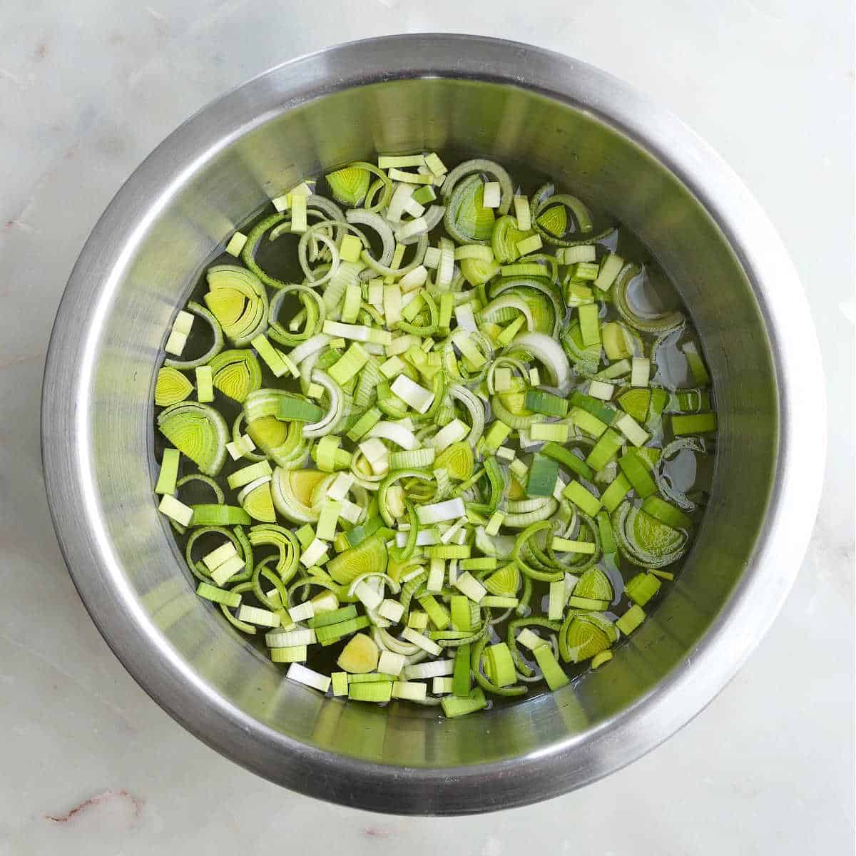 cut leeks being washed in a bowl of water on a counter
