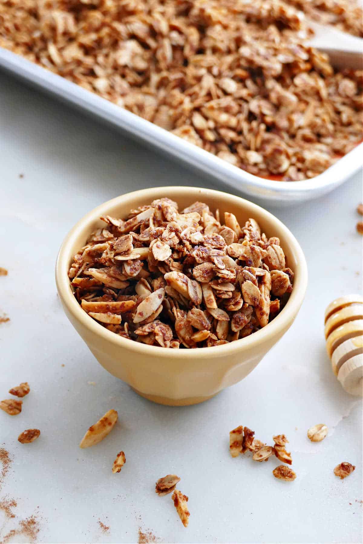 almond granola in a bowl in front of a sheet pan with granola