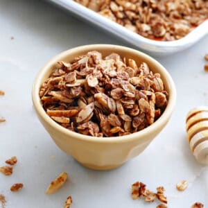almond granola in a bowl in front of a sheet pan with granola