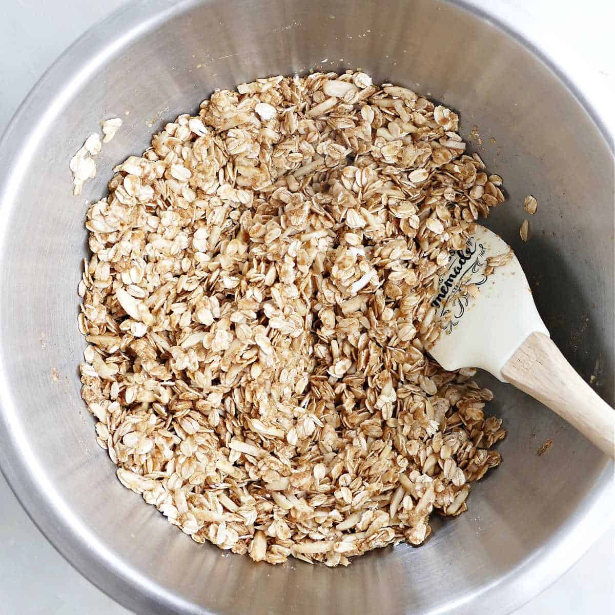 ingredients for almond granola being mixed together with a rubber spatula