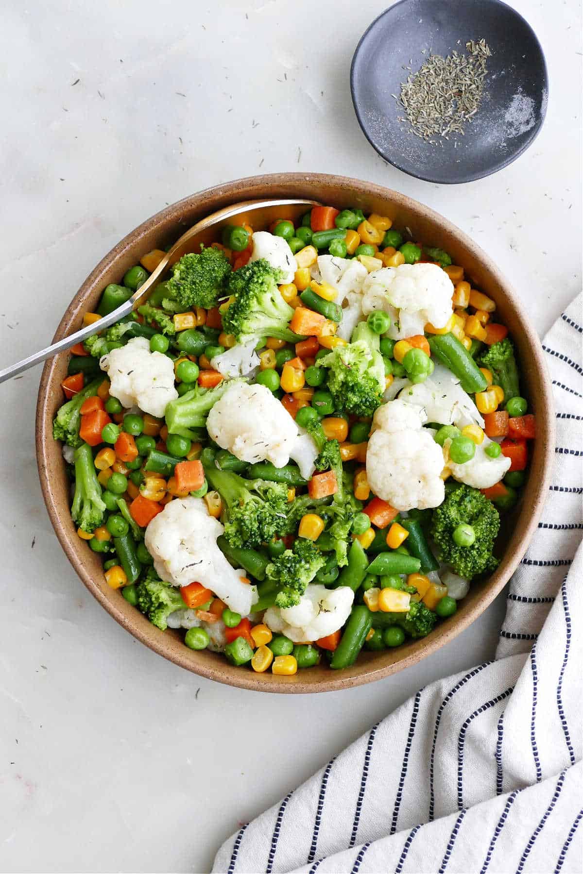 buttered vegetables in a serving bowl next to a napkin and spices