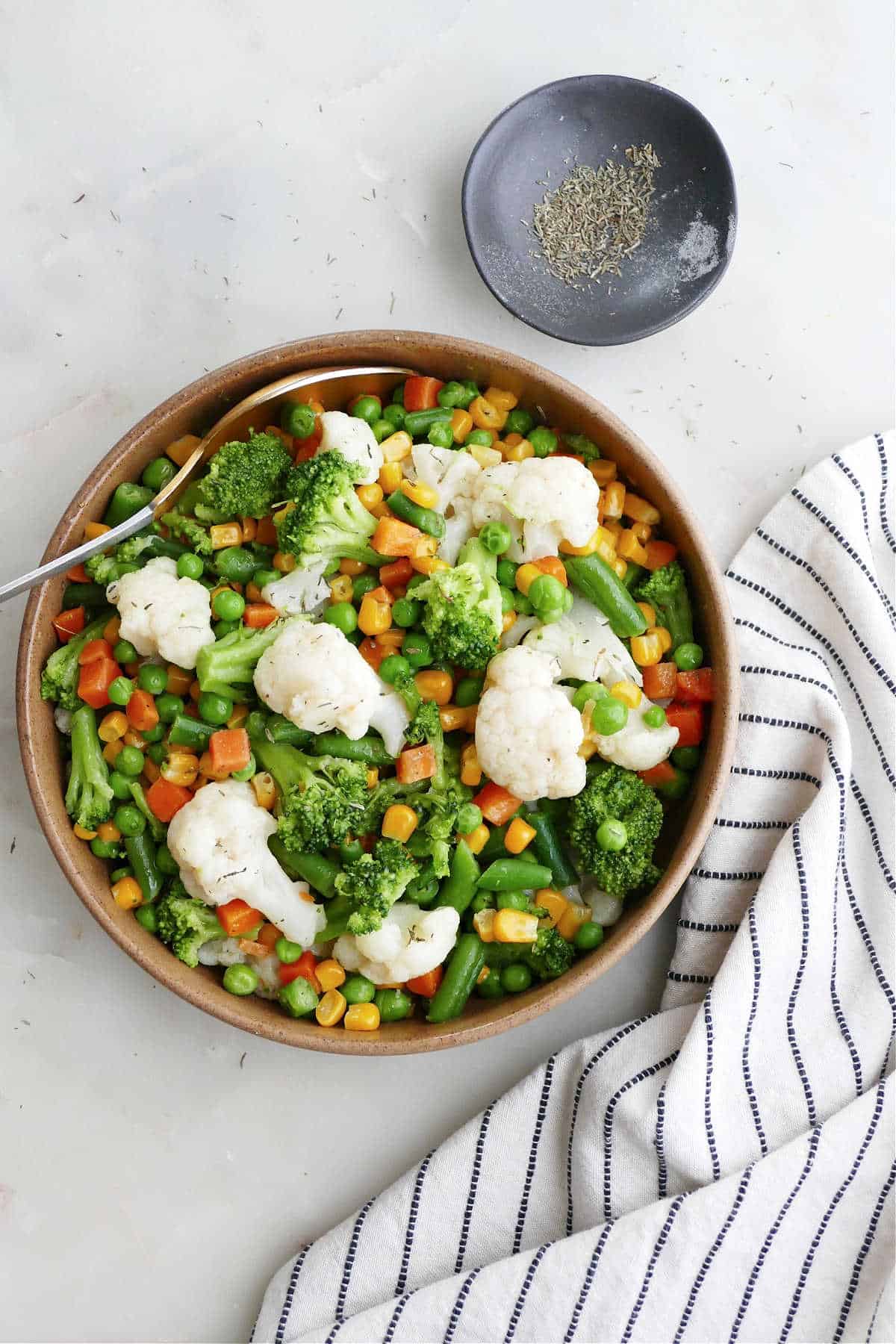 buttered vegetables in a serving bowl next to a napkin and spices