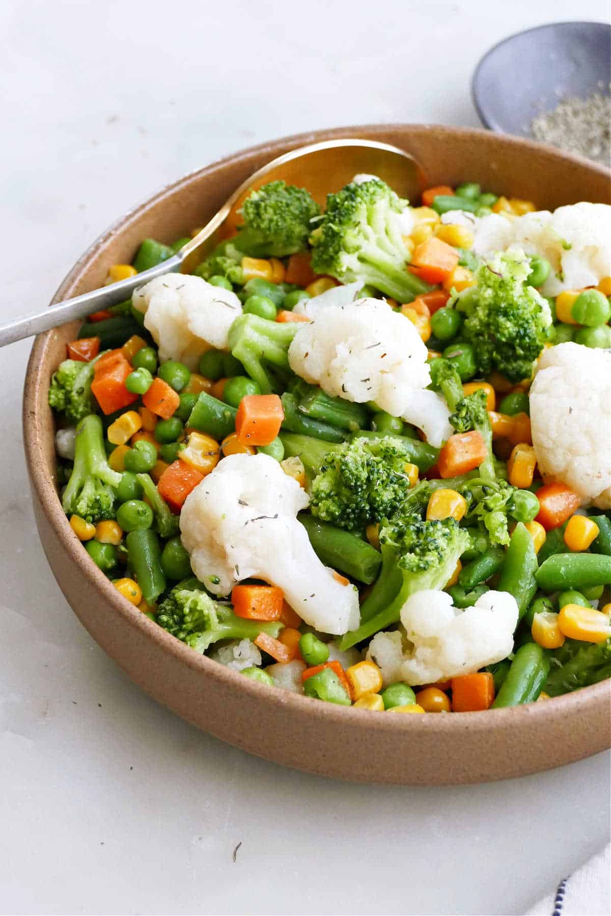 cauliflower, broccoli, carrots, green peans, corn, and peas, tossed in a butter in a bowl