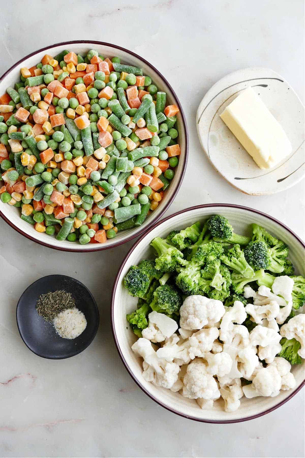 frozen mixed vegetables, broccoli, and cauliflower in bowls next to butter and spices