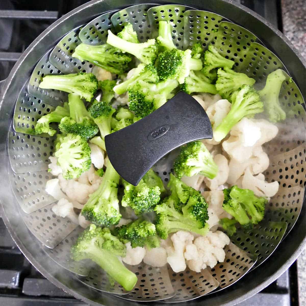 broccoli and cauliflower cooking in a vegetable steamer basket over a pot
