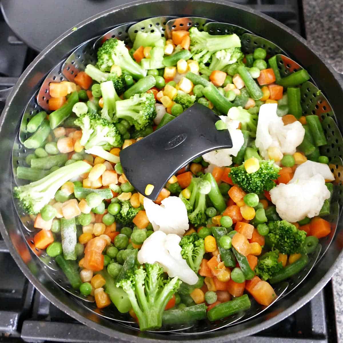 mixed vegetables cooking in a steamer basket over a pot