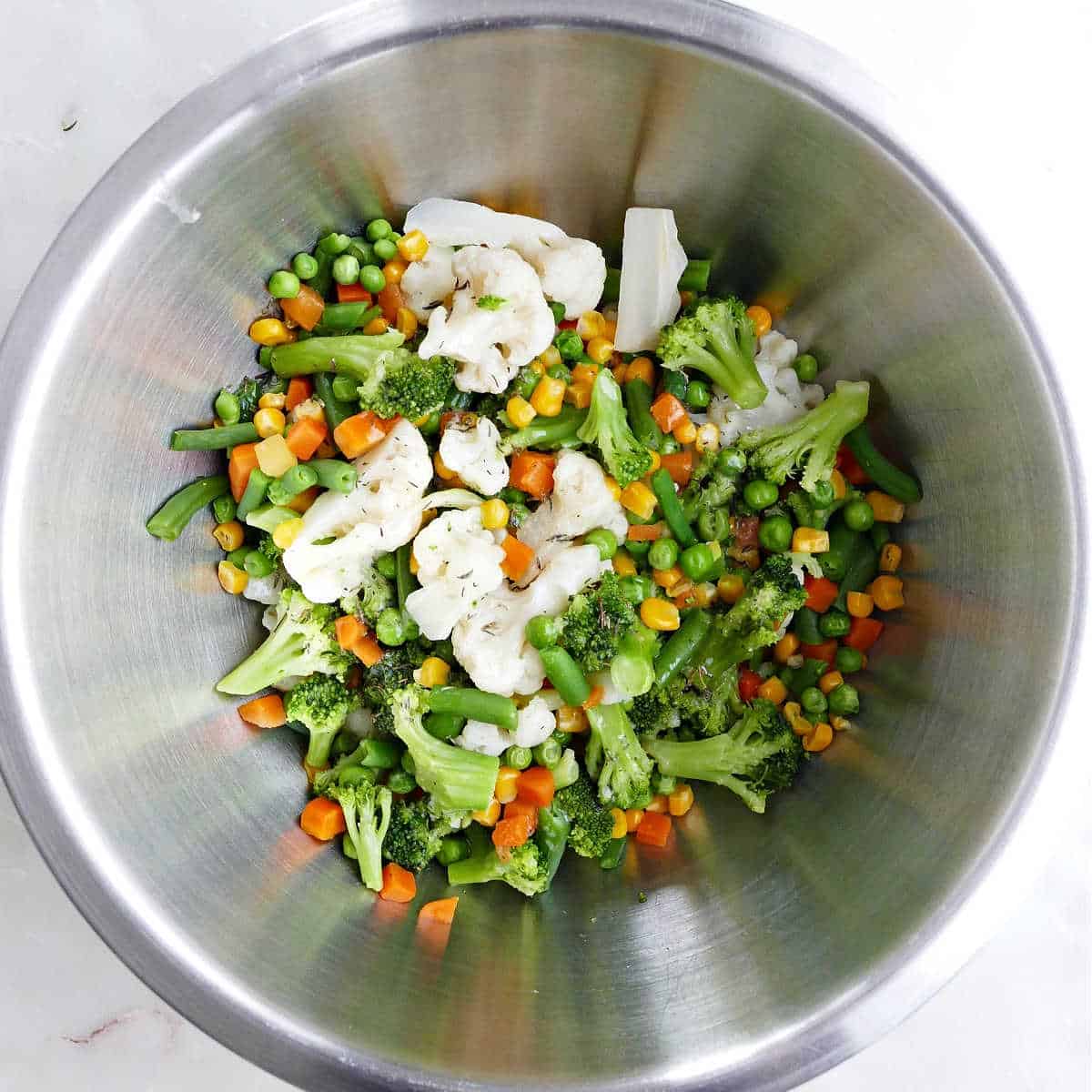 steamed vegetables tossed with melted butter and seasonings in a bowl