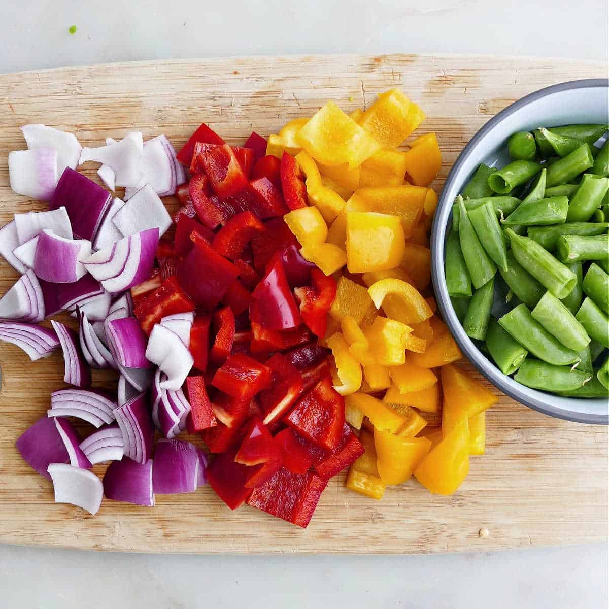 sliced red onion, bell peppers, and sugar snap peas on a cutting board