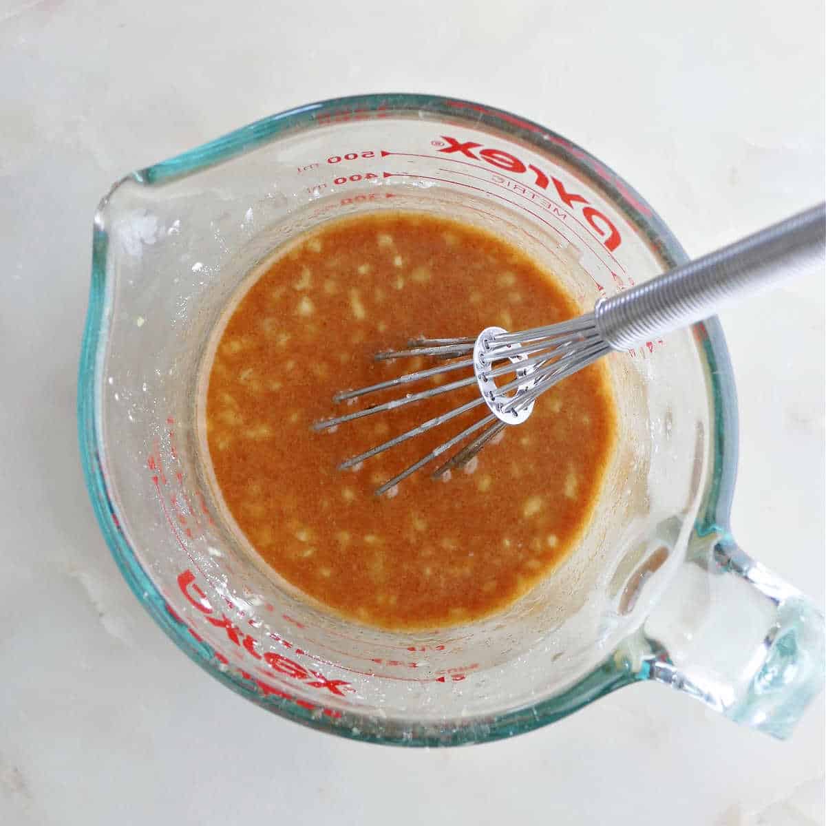 ingredients for pineapple stir fry sauce being whisked together in a measuring cup