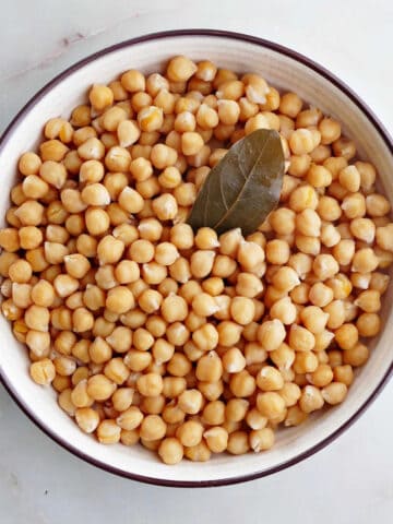cooked chickpeas in a serving bowl with a bay leaf