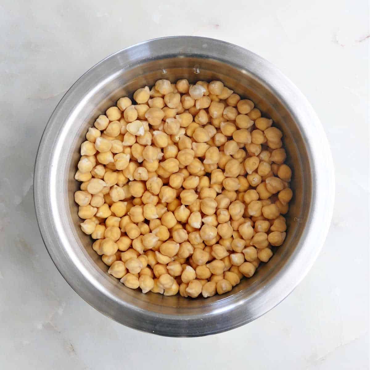 dried garbanzo beans soaking in a bowl of water on a counter