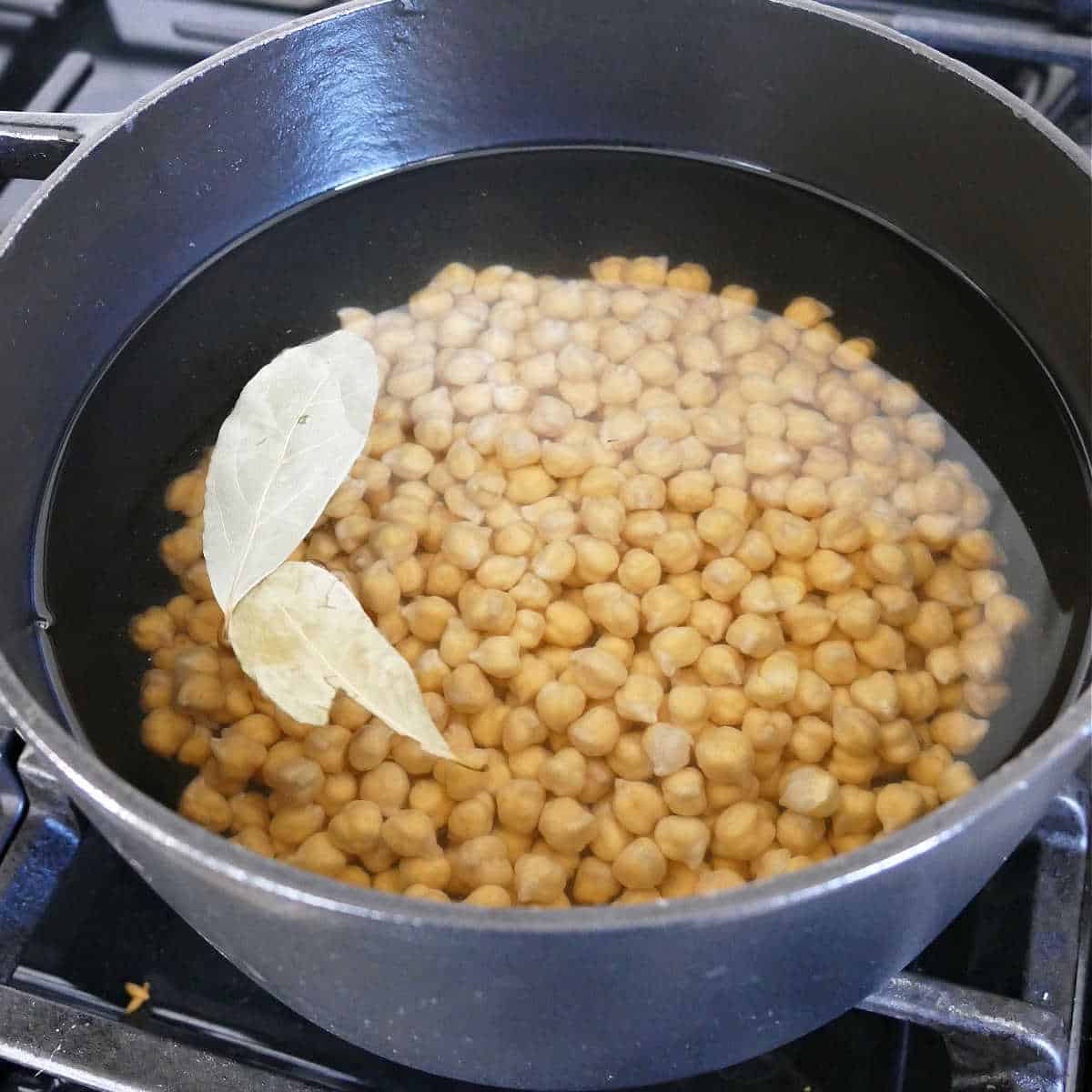 dried chickpeas cooking in a pot on the stove with bay leaves