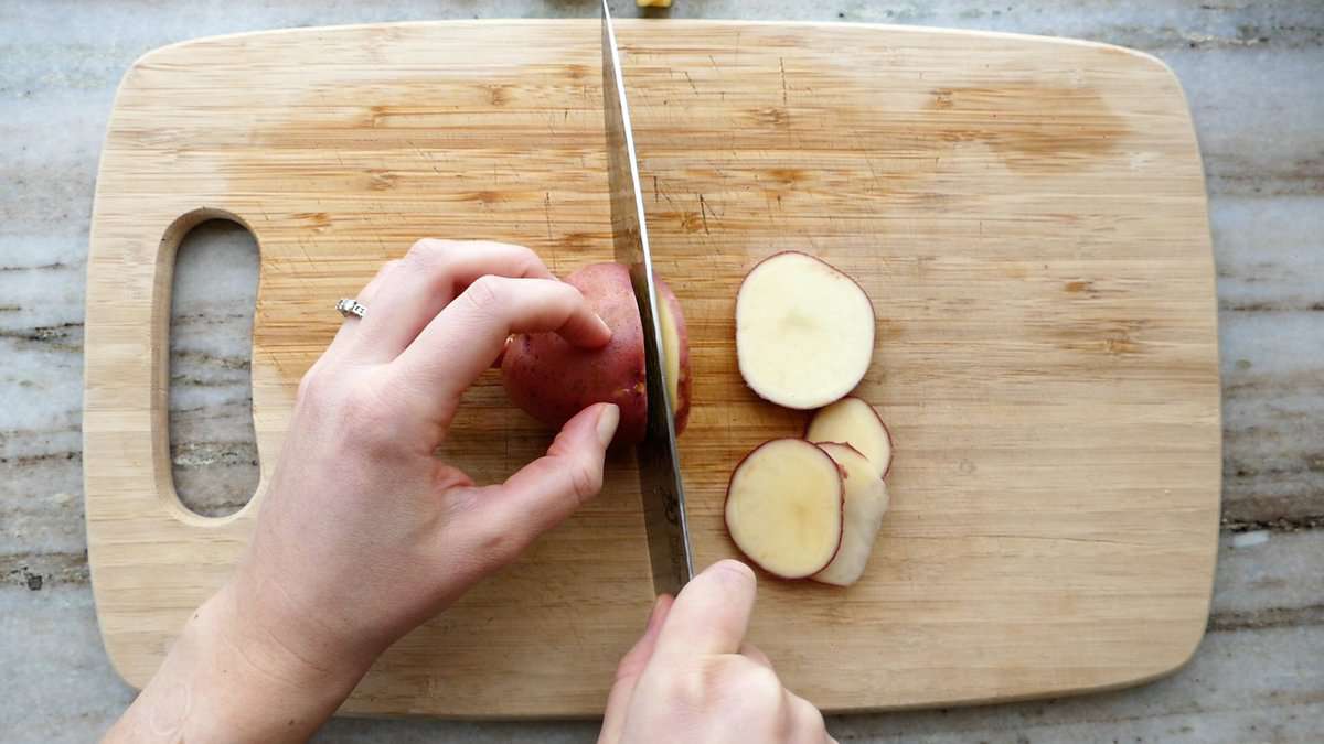 woman slicing a red potato on a cutting board