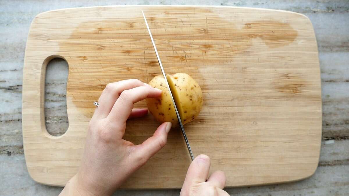 woman cutting a yellow potato in half on a cutting board