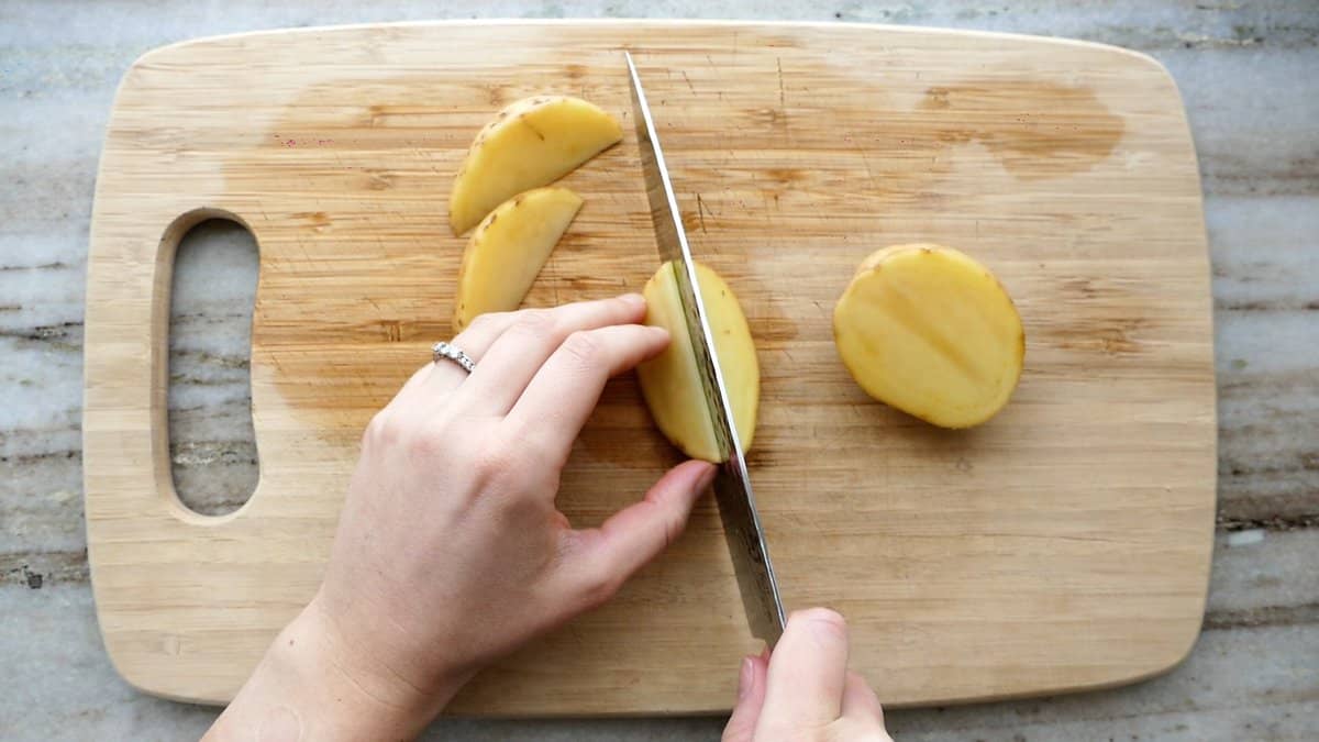 woman cutting a yellow potato into wedges on a cutting board