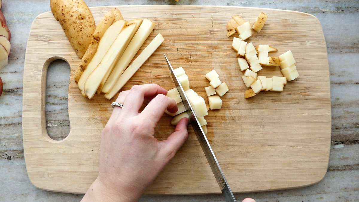 woman cutting a potato into cubes on a cutting board