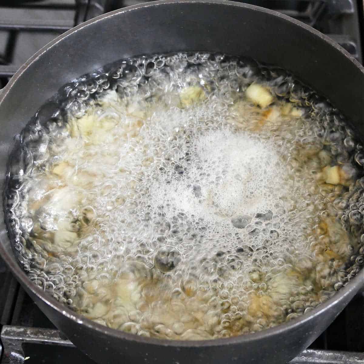 potatoes being blanched in a pot of boiling water on a stove