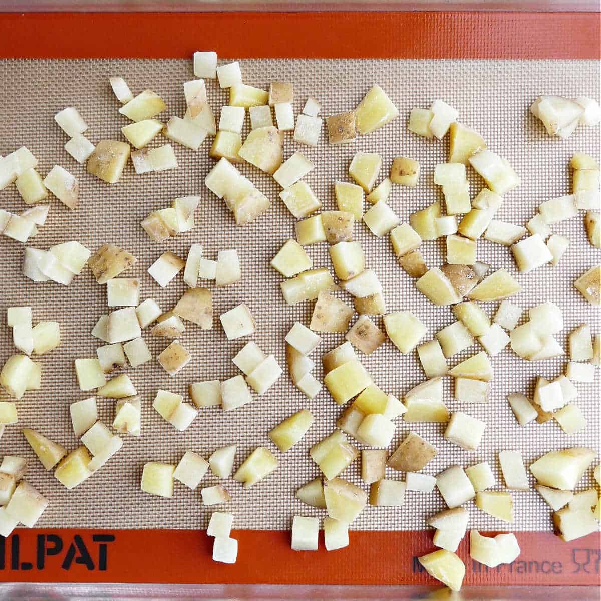 blanched potato cubes spread out on a baking sheet lined with a silicone mat
