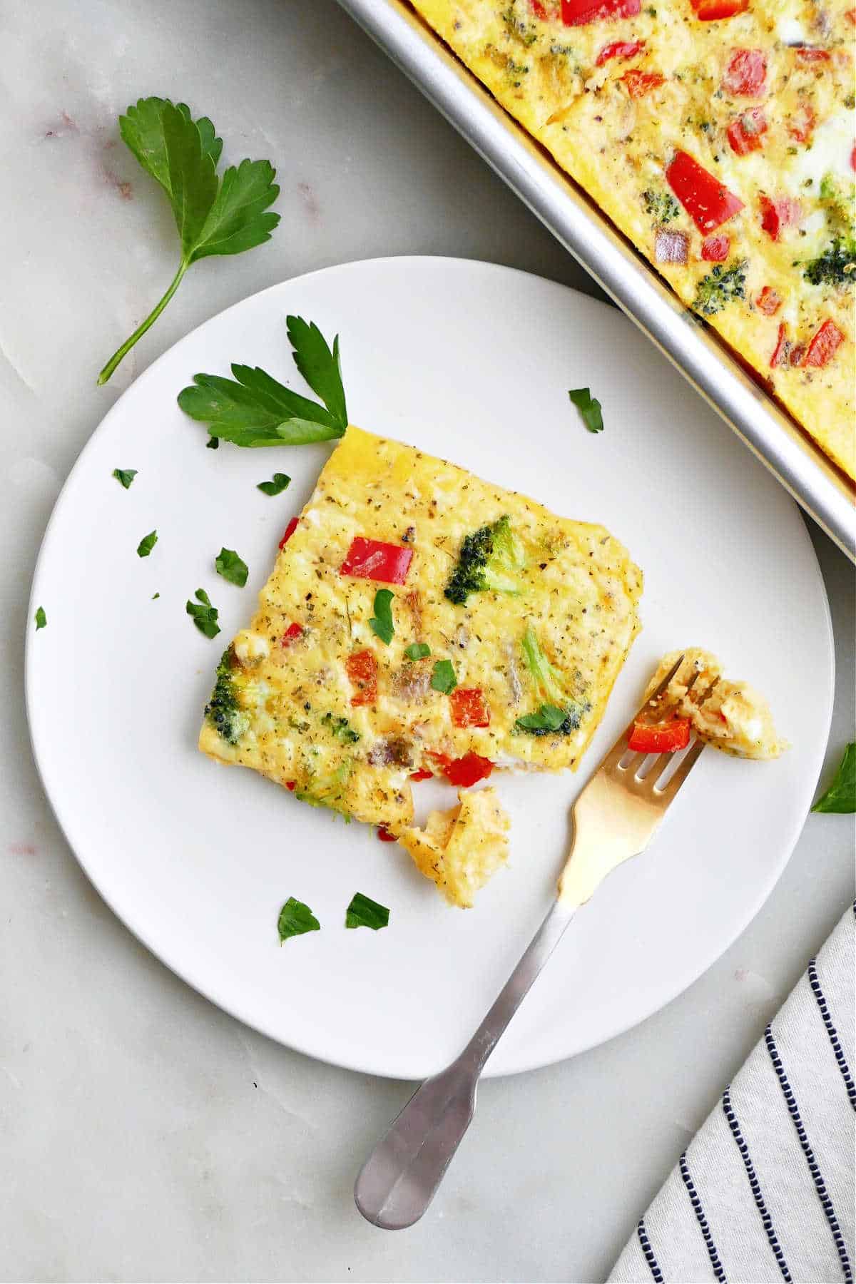 slice of a sheet pan veggie omelet on a plate next to the baking sheet