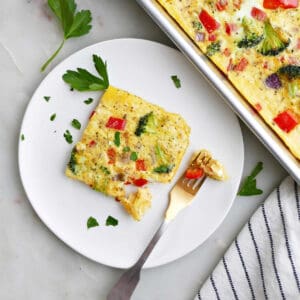slice of a sheet pan veggie omelet on a plate next to the baking sheet