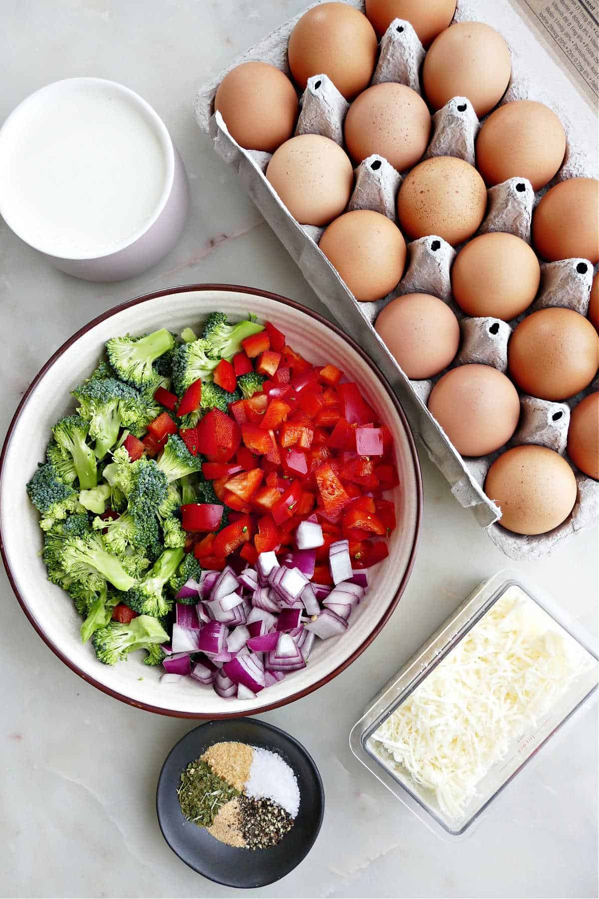 milk, eggs, veggies, shredded cheese, and spices on a counter