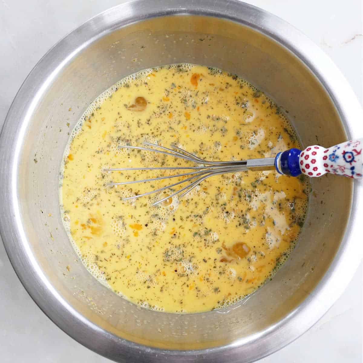 eggs, cheese, milk, and spices being whisked together in a mixing bowl