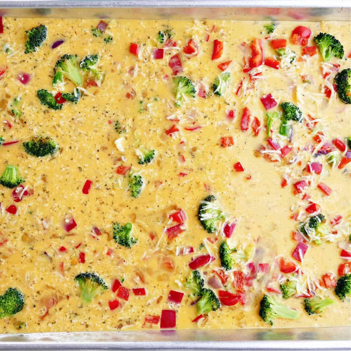 egg mixture poured over vegetables on a half sheet pan before baking