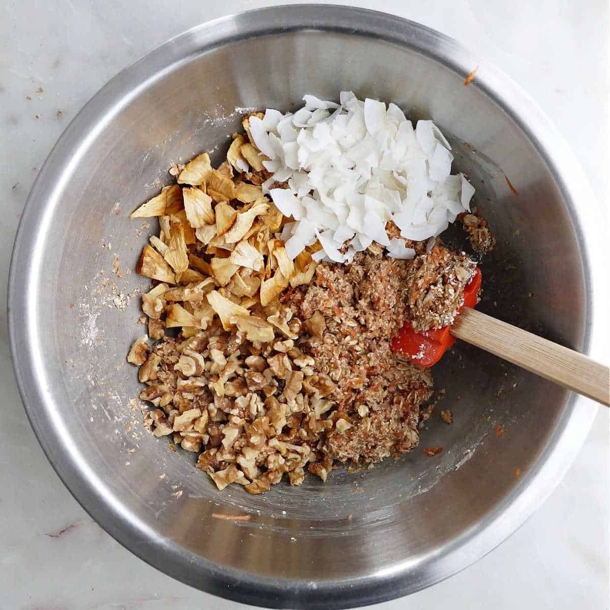 morning glory cookie batter with coconut, dried pineapple, and walnuts being folded into it