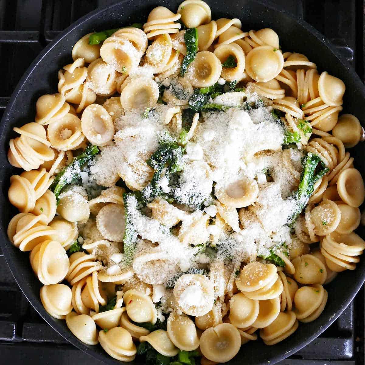 orecchiette pasta mixed with broccoli rabe and grated cheese in a skillet