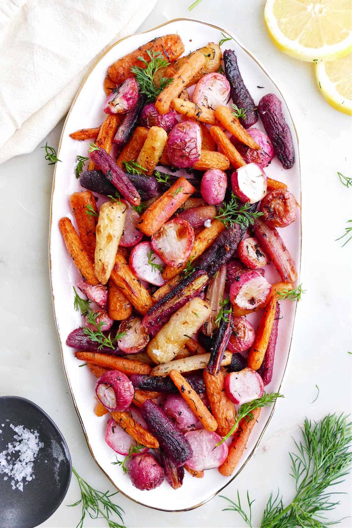 roasted radishes and carrots on a serving dish surrounded by toppings