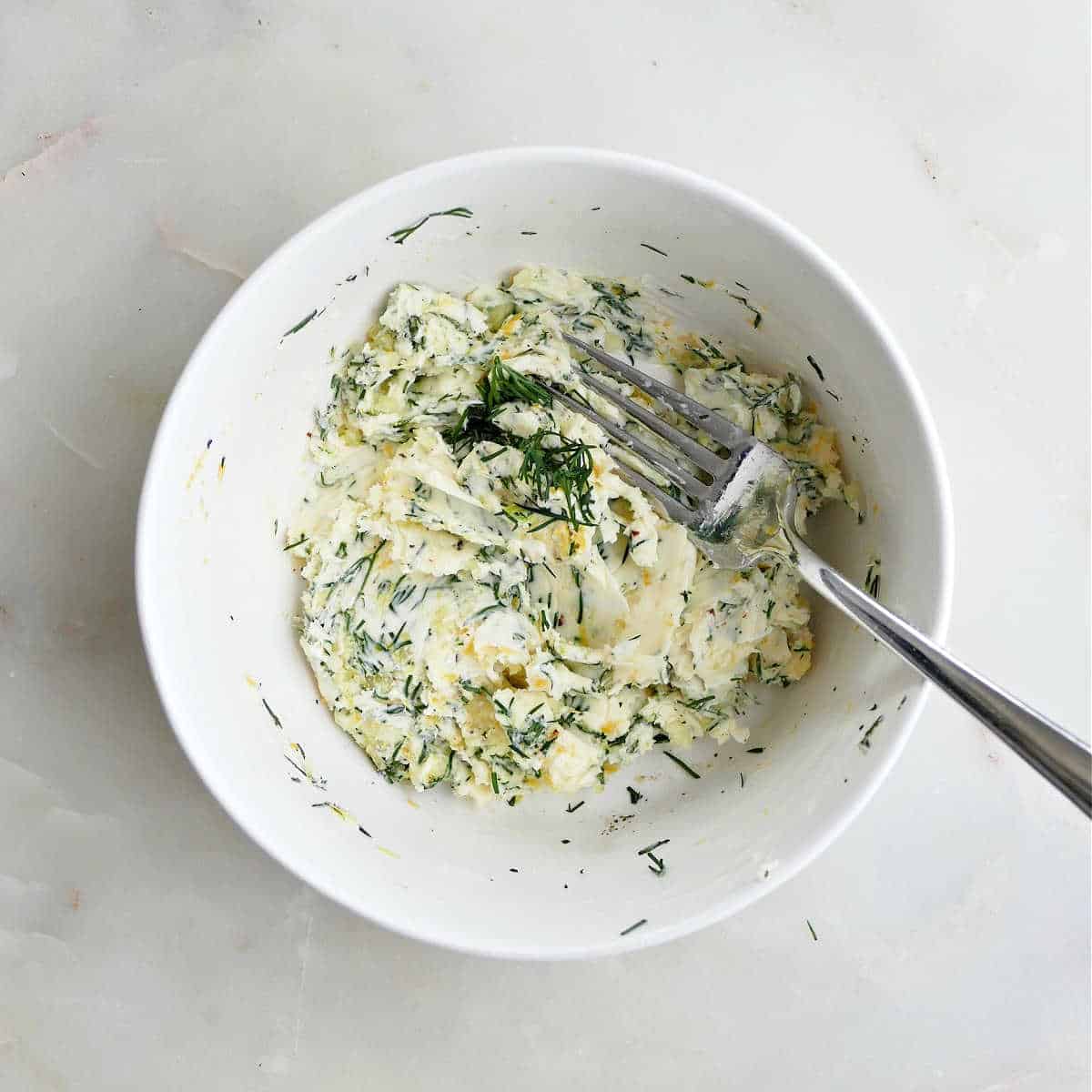 butter being mixed with lemon, garlic, and chopped dill in a bowl